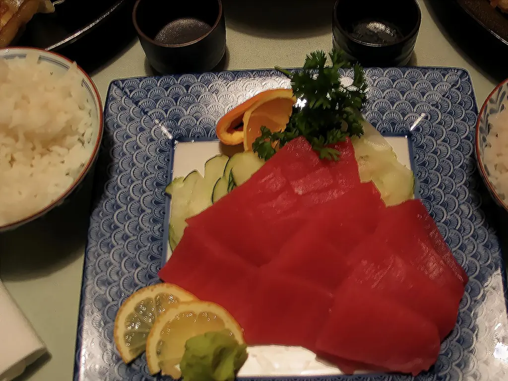 Slices of red tuna sashimi on a blue plate printed with waves with lemon and wasabi