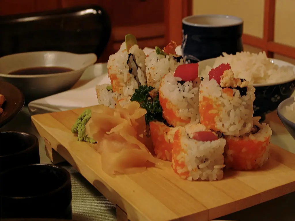 Sushi rolls topped with orange roe on a wooden geta board with pickled ginger and wasabi