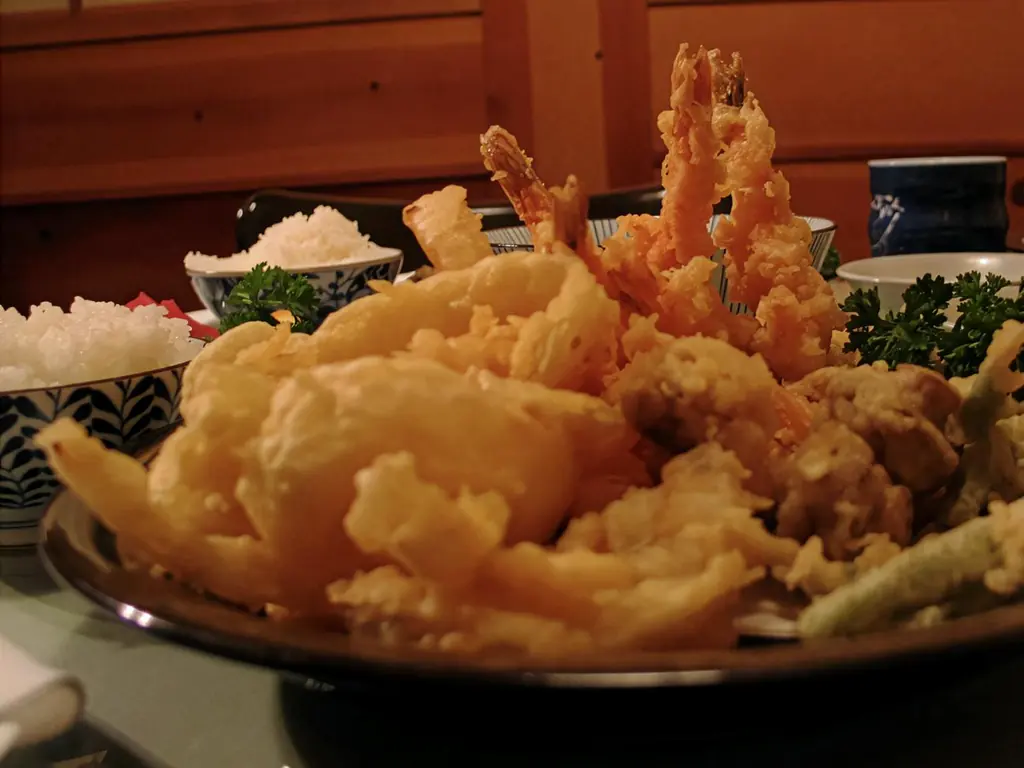 A platter of golden shrimp and vegetable tempura with rice and blue patterned tea cups