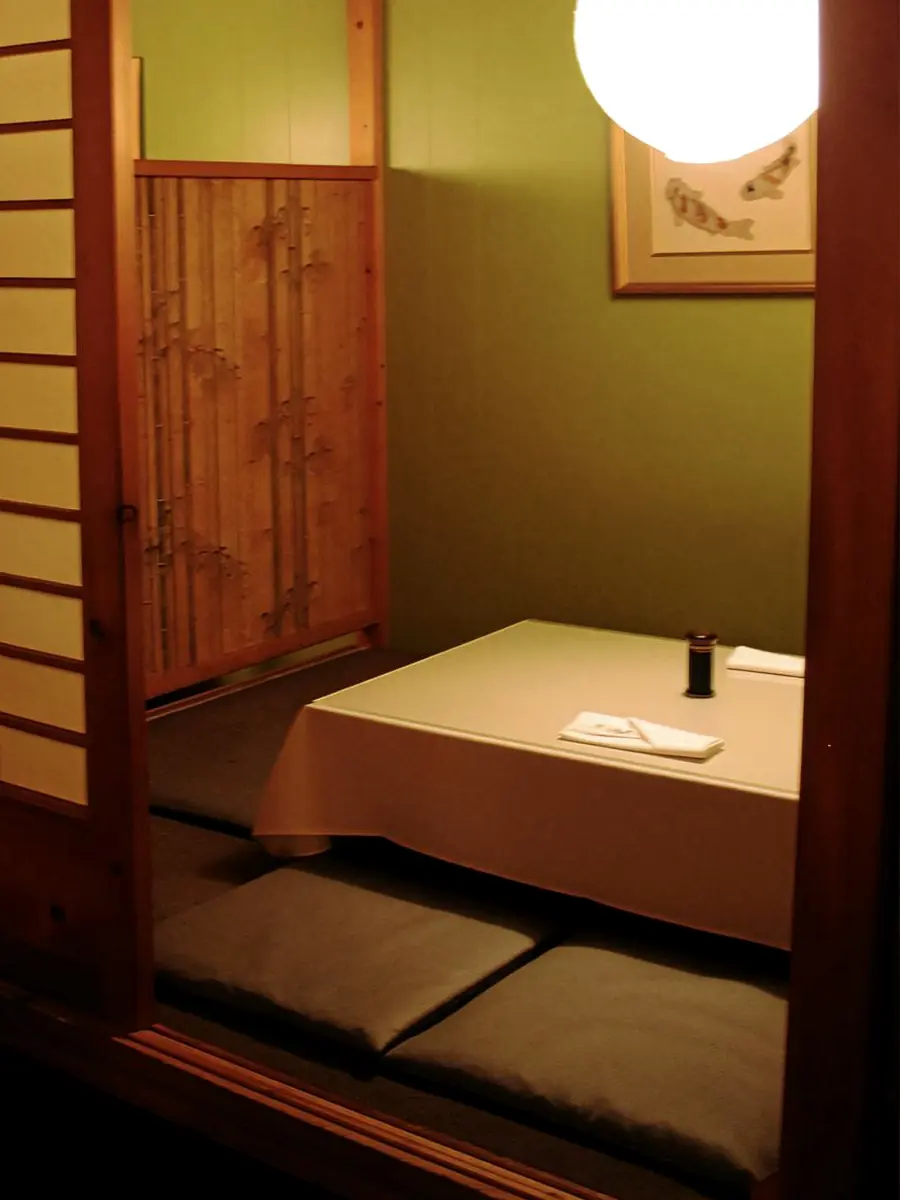 A private zashiki room behind a shoji screen: a low table on tatami with floor cushions and a bamboo print panel